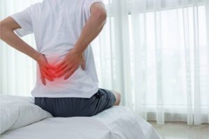 Un uomo seduto a letto col mal di schiena