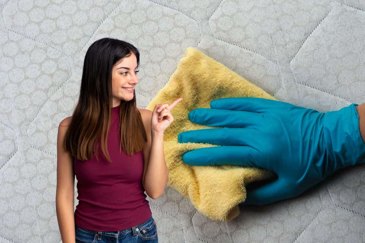 mano con guanto che passa pezza sul materasso, donna che indica