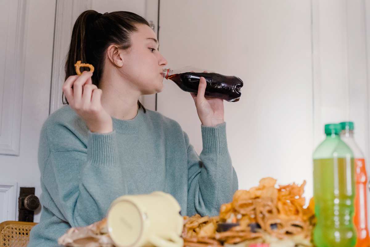 ragazza beve coca cola e mangia cibo fritto